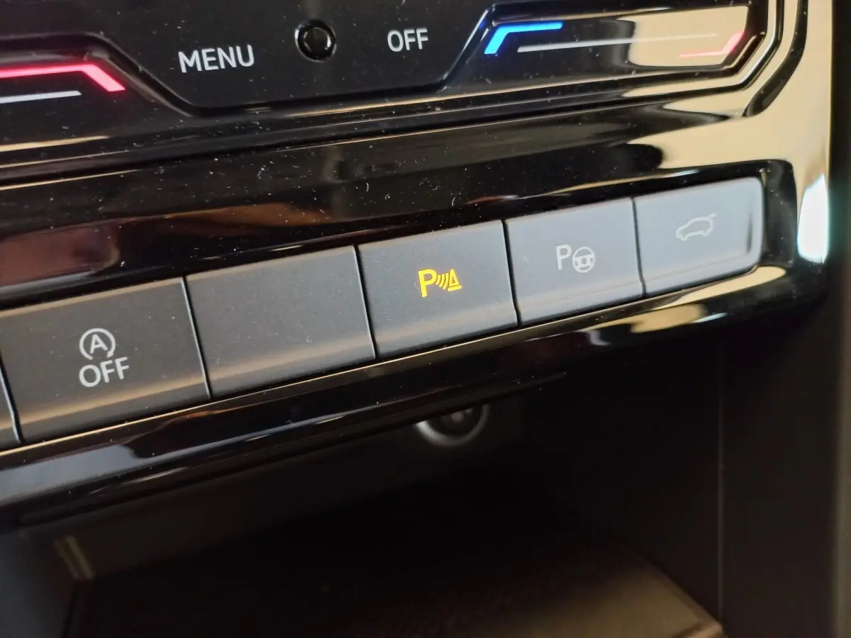 Gros plan sur les boutons de commande du tableau de bord noir du Volkswagen Touran 2024, avec témoin d'aide au stationnement allumé.