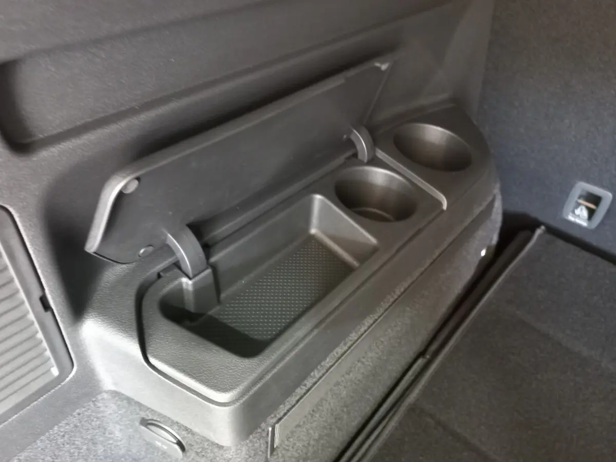 Détail du rangement avec porte-boissons intégré dans le coffre noir du Volkswagen Touran 2024, côté droit.
