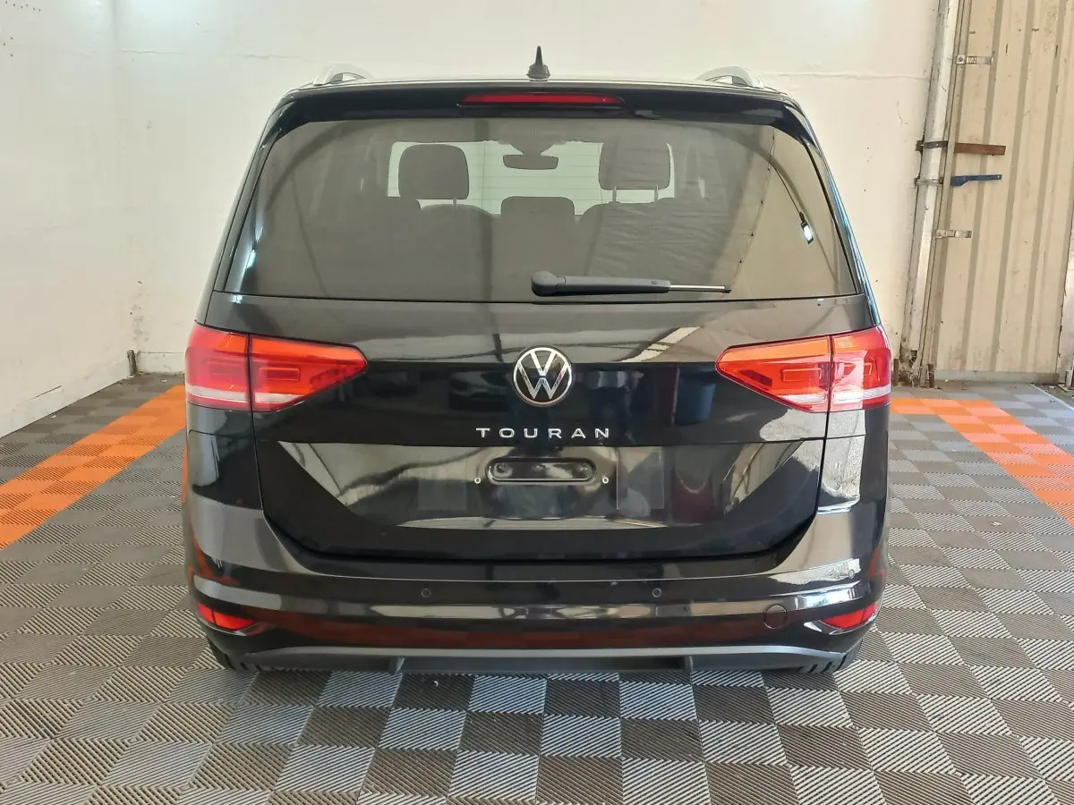 Vue arrière d’un Volkswagen Touran noir 2024 avec feux arrière rouges et logo central visible.