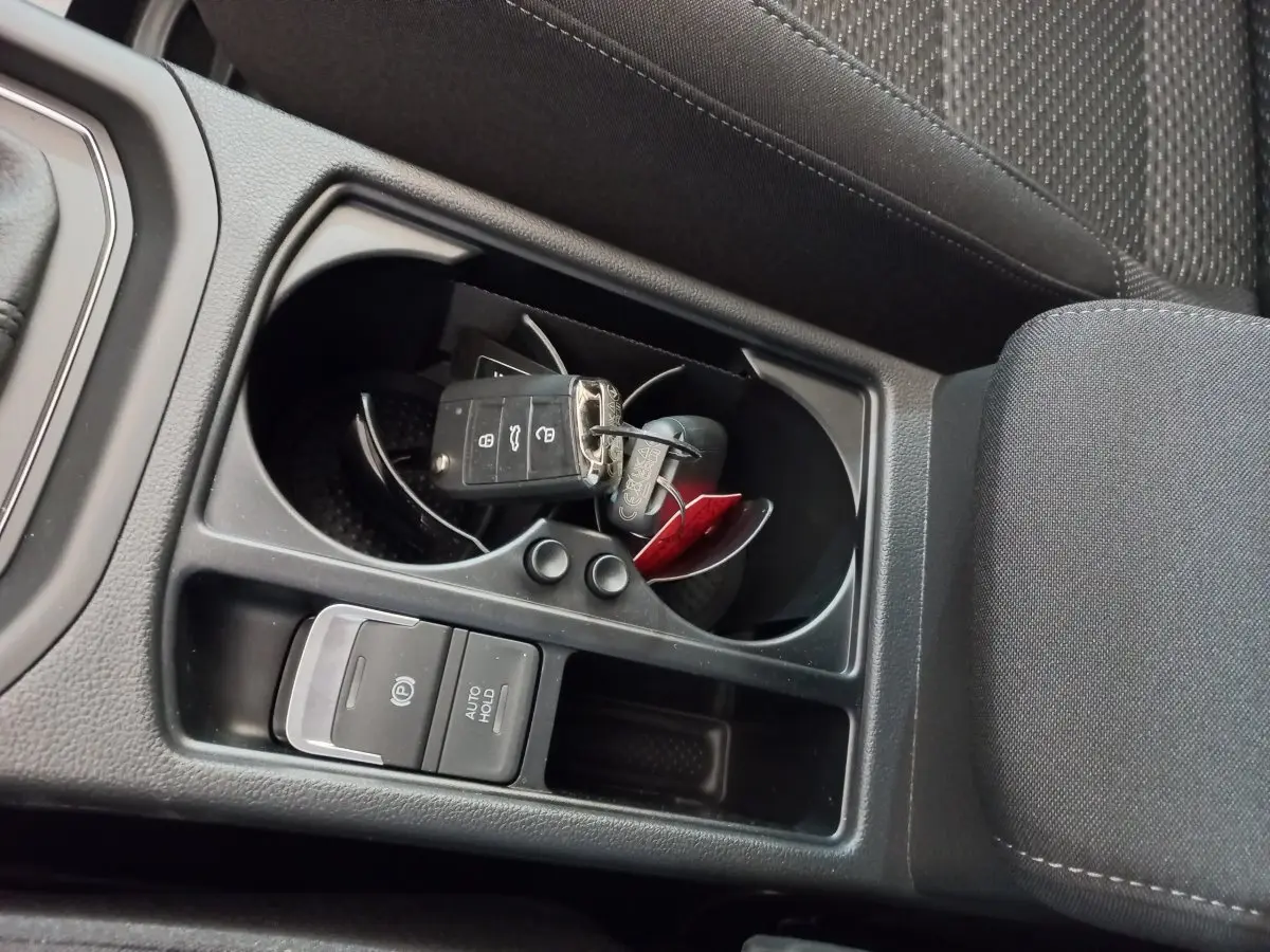 Gros plan sur la console centrale noire du Volkswagen Touran 2024 avec clés dans porte-gobelets et frein à main électrique.