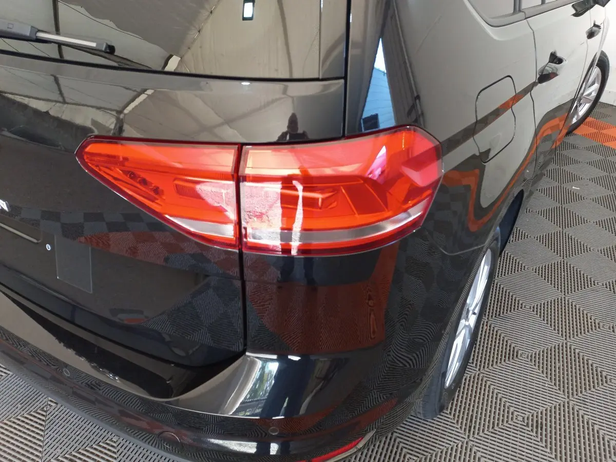 Vue arrière côté droit du Volkswagen Touran noir 2024, mettant en valeur le feu arrière et la carrosserie brillante.