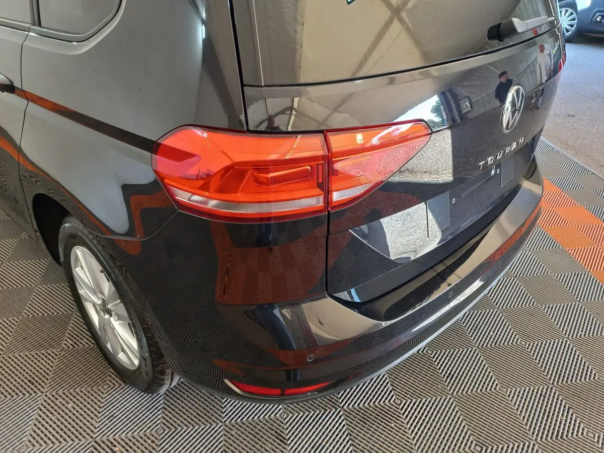 Vue 3/4 arrière droite d’un Volkswagen Touran noir 2024 avec feux arrière rouges et logo VW visible.
