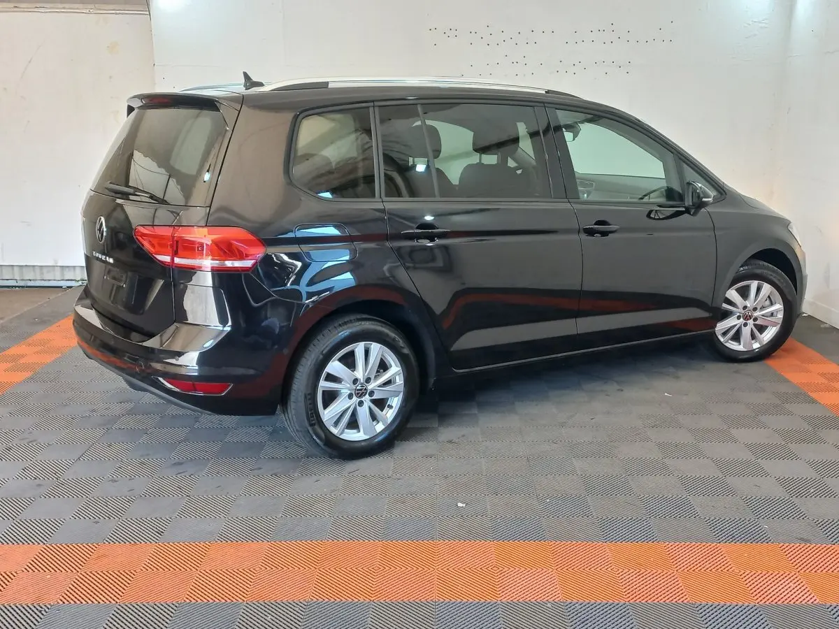 Volkswagen Touran noir vu de profil côté droit dans un intérieur avec sol gris et bandes orange.