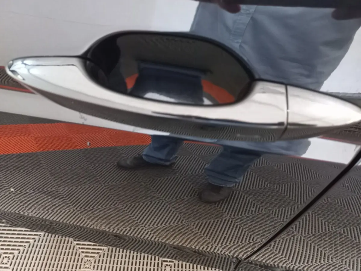 Poignée de porte chromée en gros plan sur la porte côté droit d’un Volkswagen Touran noir 2024.