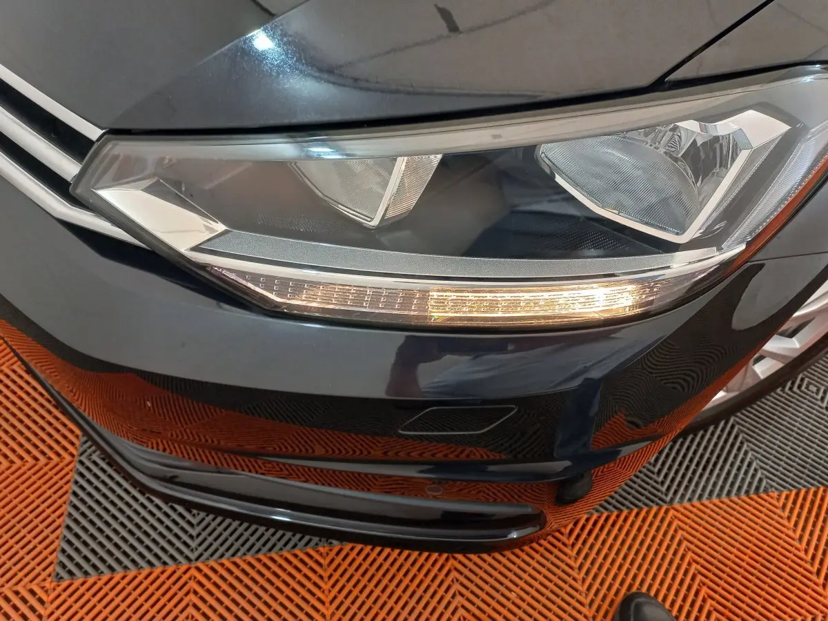 Gros plan sur le phare avant droit d’un Volkswagen Touran noir 2024 avec clignotant allumé.