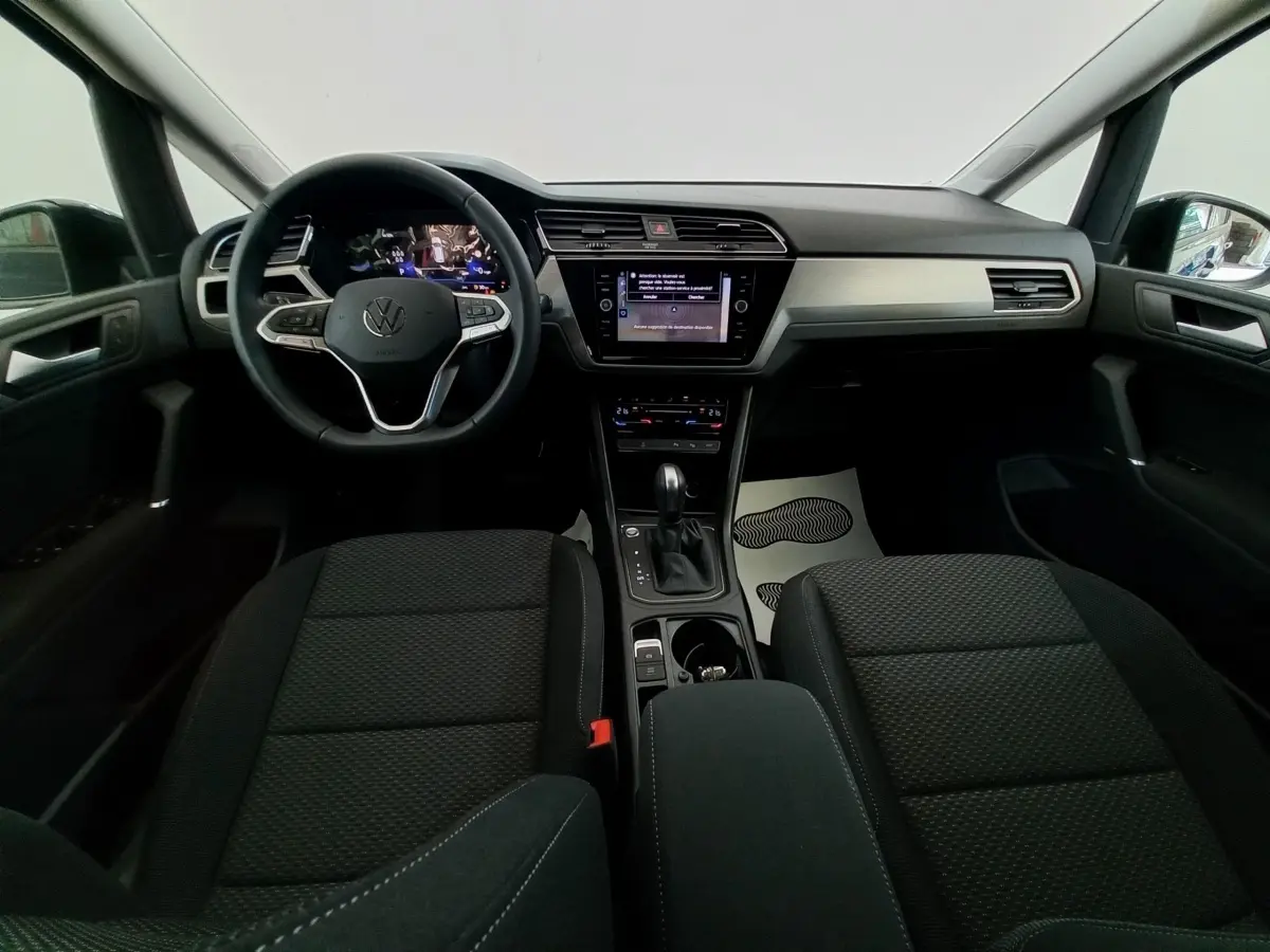 Vue intérieure avant du Volkswagen Touran 2024 noir, tableau de bord moderne avec écran tactile central et volant multifonctions.