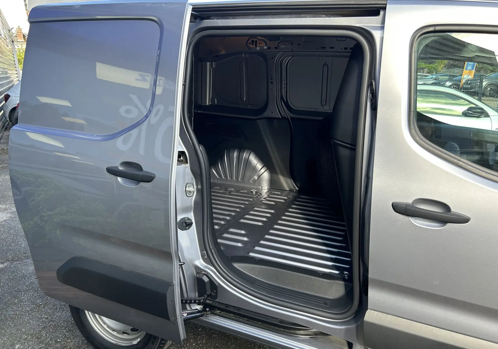 Vue latérale gauche du Peugeot Partner Dangel gris Artense avec porte coulissante ouverte dévoilant l’espace de chargement vide.