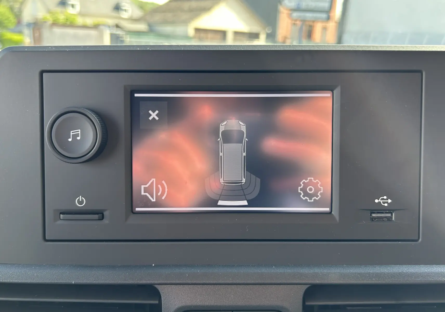 Écran tactile intérieur du DANGEL Partner 2025 affichant l'aide au stationnement avec vue du véhicule en gris Artense.