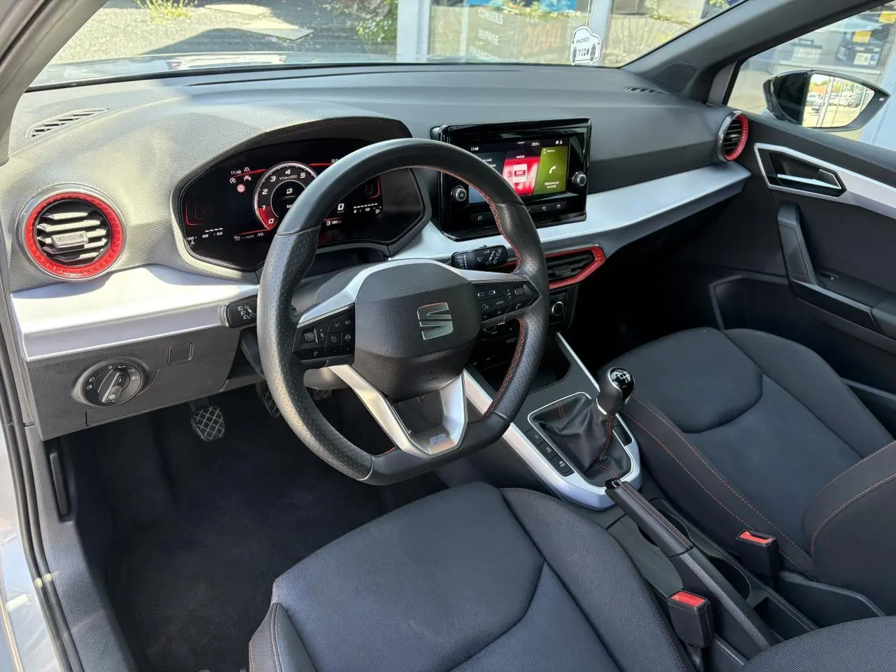 Vue intérieure côté conducteur du SEAT Arona 2024 FR, volant cuir sport, tableau de bord digital et sellerie textile noire.