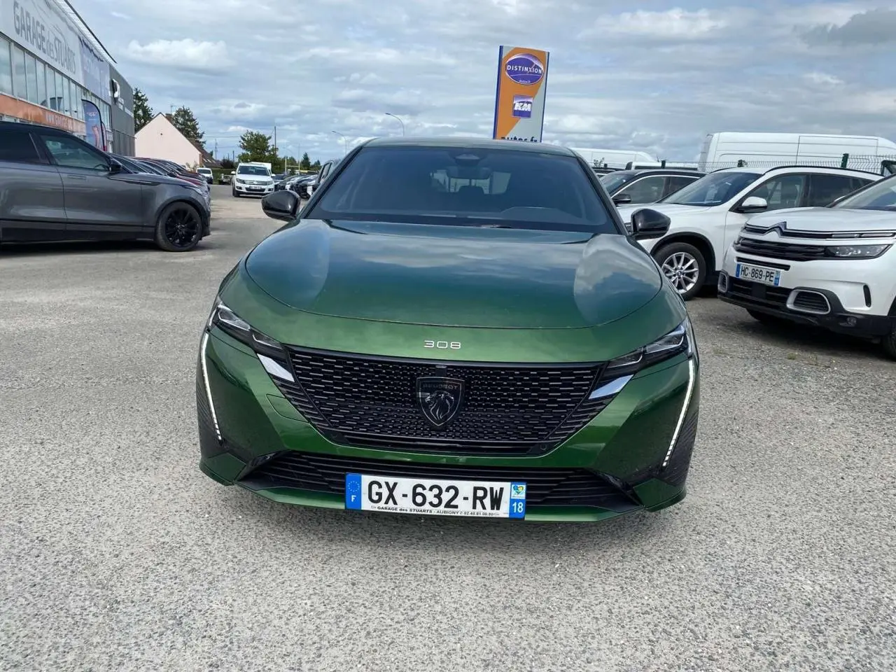 Vue avant d'une Peugeot 308 2023 vert olivine avec calandre noire et feux LED verticaux allumés.