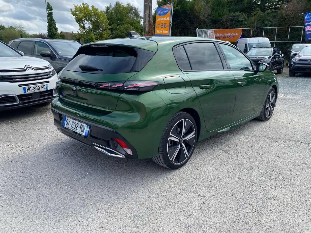 Peugeot 308 GT vert olivine vue 3/4 arrière droit sur parking avec jantes alliage et vitres teintées.