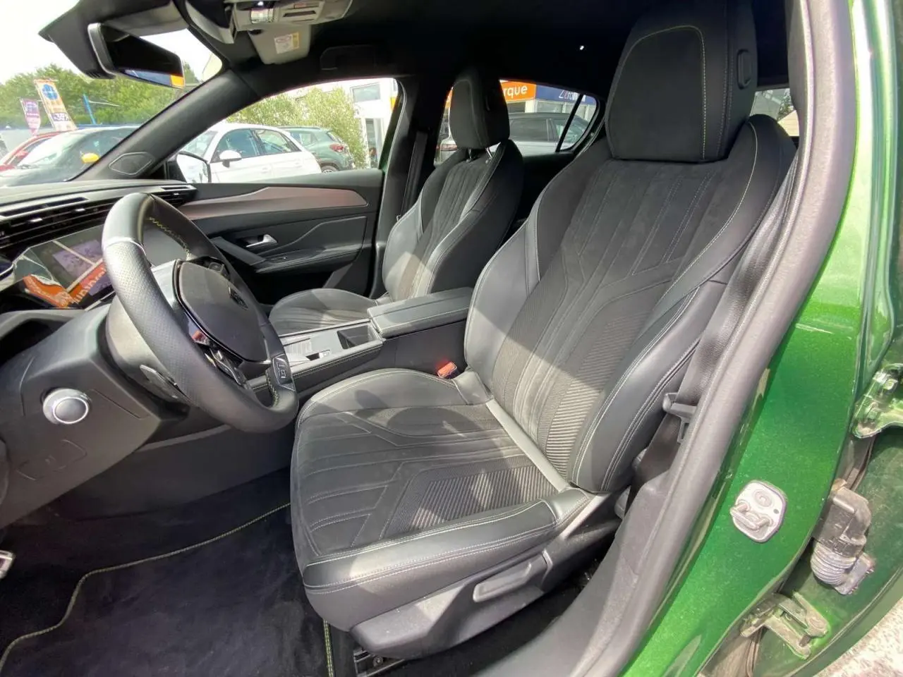 Vue intérieure côté conducteur de la Peugeot 308 2023 vert olivine, avec sièges en tissu et cuir noir et tableau de bord moderne.