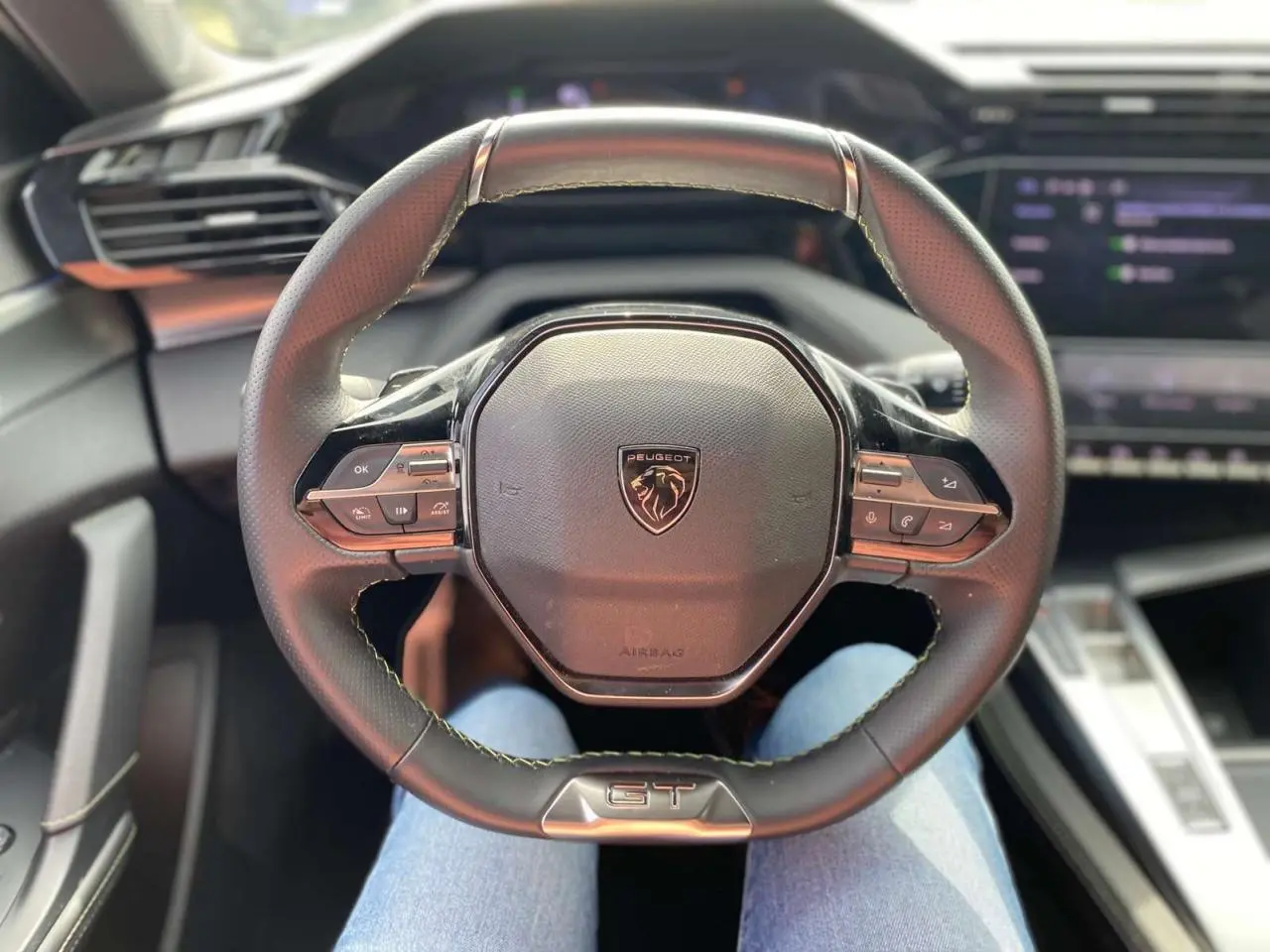 Volant cuir GT de la Peugeot 308 2023 vu de face, avec commandes intégrées et tableau de bord numérique flou.
