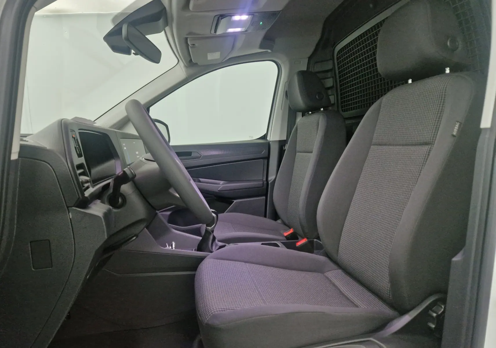 Vue intérieure côté conducteur du Volkswagen Caddy Maxi blanc 2025, montrant sièges avant et tableau de bord minimaliste.