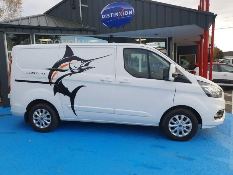 Vue de profil côté gauche du Ford Transit Custom blanc glacier avec grand marlin noir et orange sur la porte latérale.