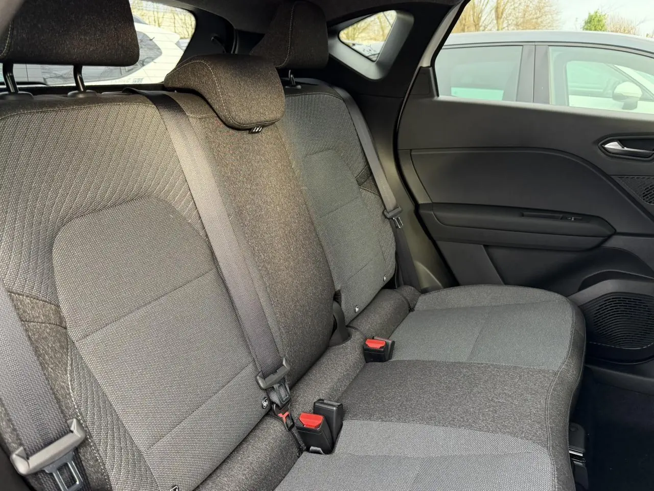 Vue intérieure côté droit des sièges arrière gris foncé du Renault Captur 2025 avec ceintures et appuie-têtes visibles.