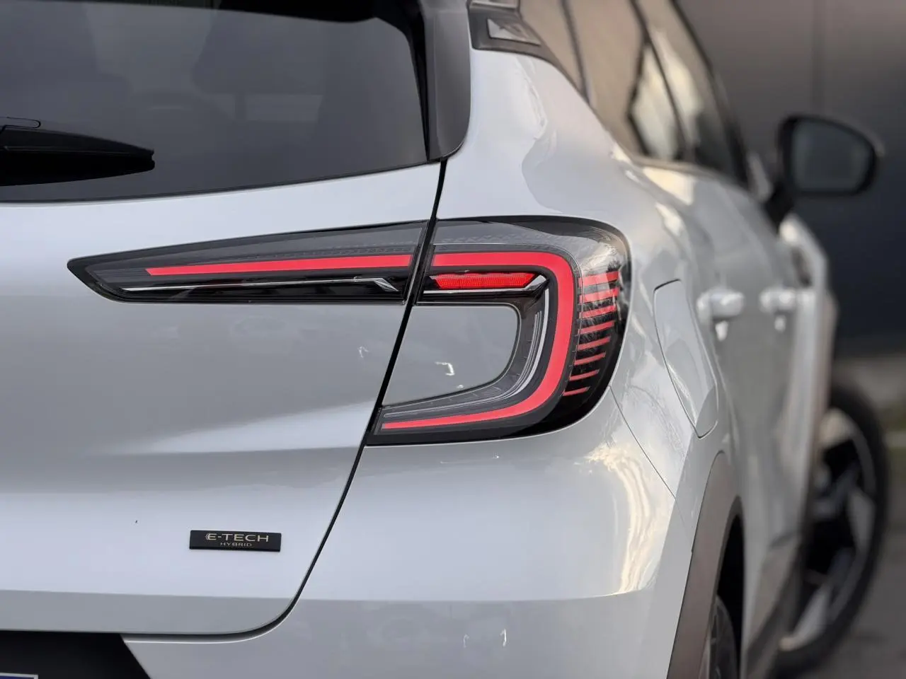 Gros plan sur l'arrière droit du Renault Captur blanc nacré, mettant en valeur le feu LED et le badge E-Tech Hybrid.