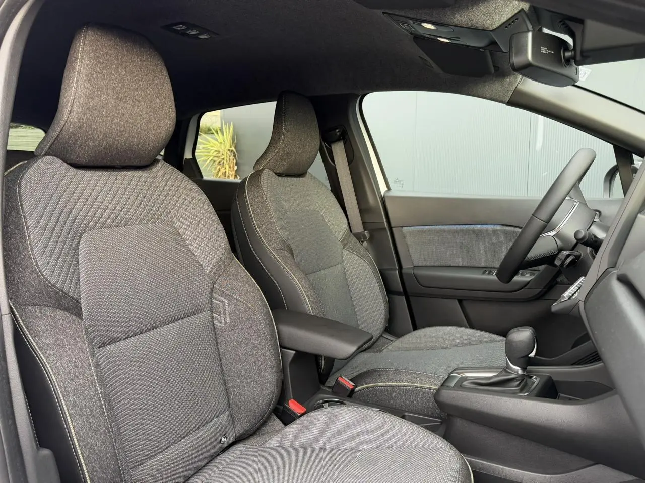 Vue intérieure côté droit du Renault Captur 2025, sièges tissu gris avec console centrale et volant visible.