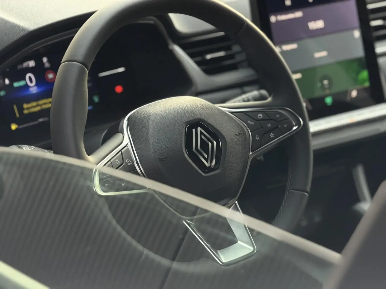 Gros plan sur le volant noir au logo Renault du Captur 2025, avec tableau de bord numérique et écran tactile visible en arrière-plan.