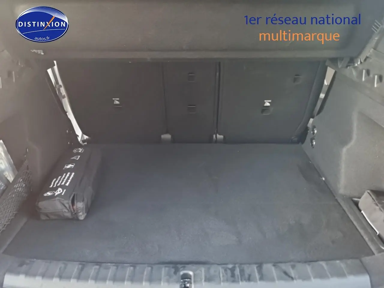 Coffre ouvert d’un BMW X1 blanc mineral, vue de l’arrière montrant un espace de chargement propre et un kit de sécurité noir.