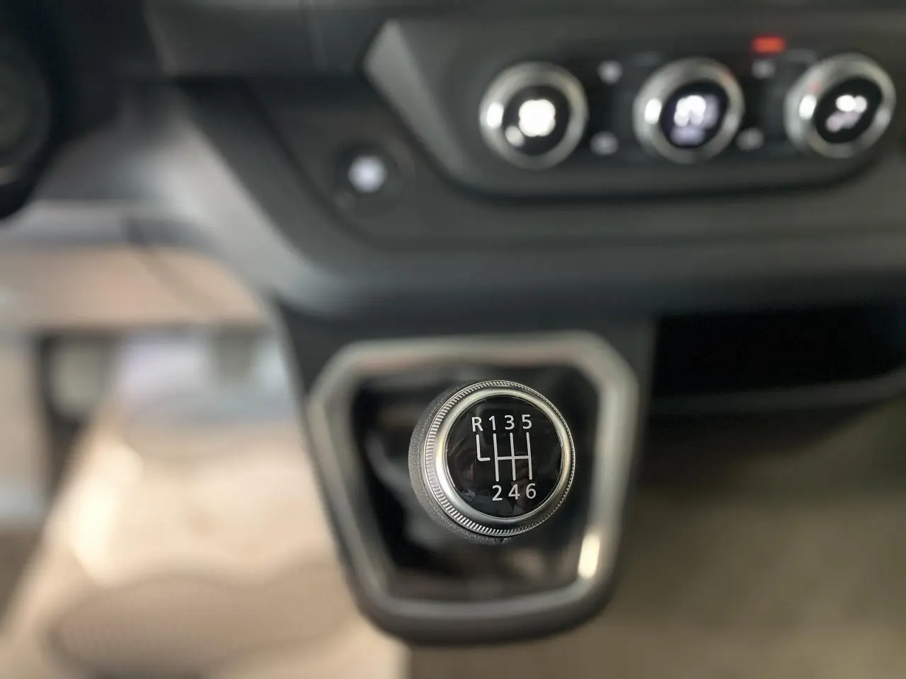 Gros plan sur le levier de vitesses manuel du Renault Trafic Fourgon gris, avec commandes de climatisation en arrière-plan flou.