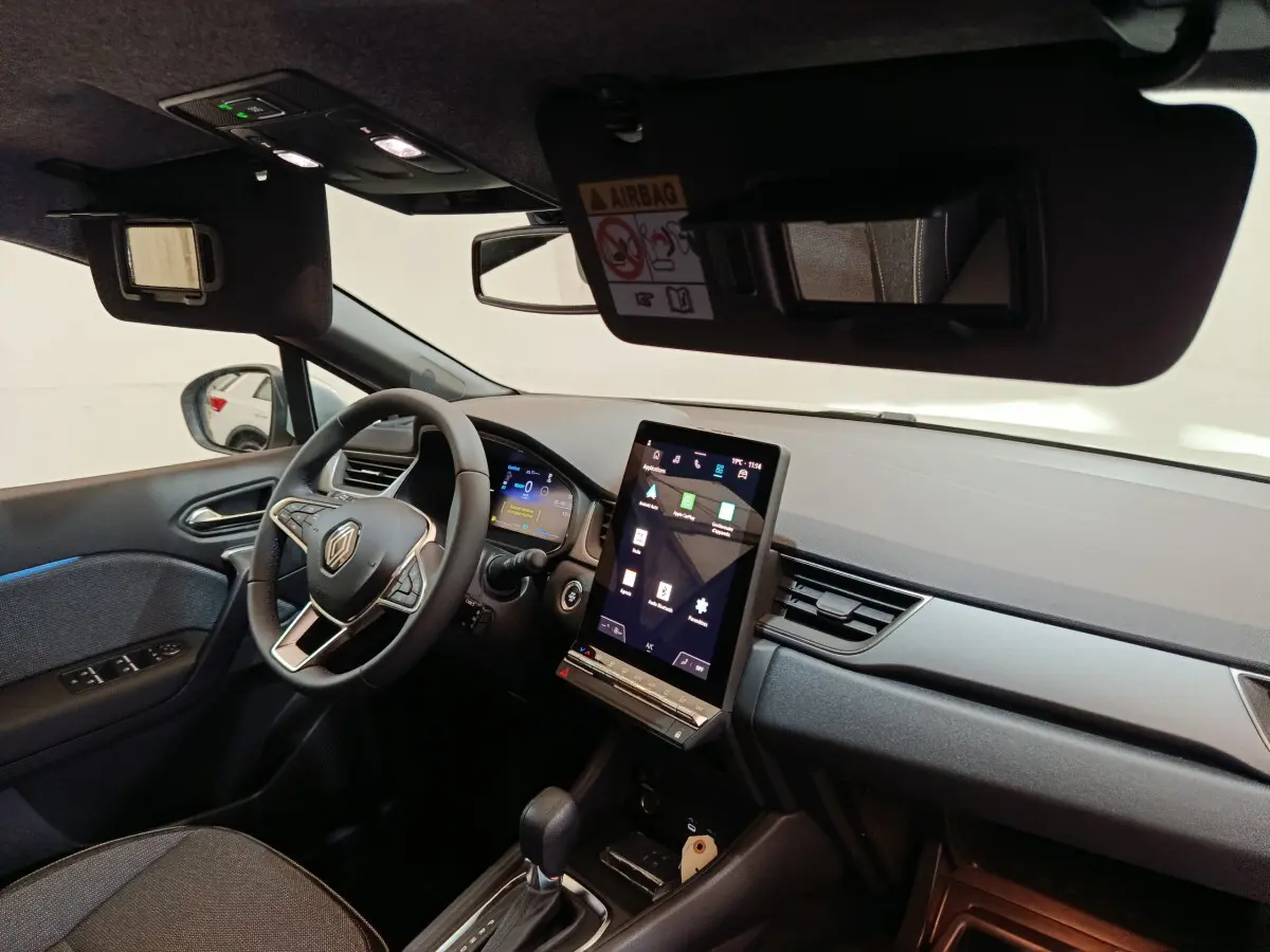 Vue intérieure côté conducteur du tableau de bord noir du Renault Captur blanc avec écran tactile vertical et volant multifonctions.