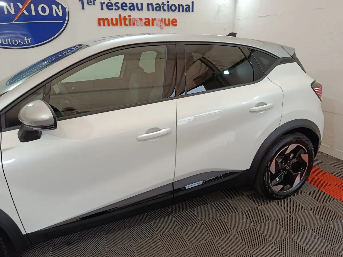 Vue de profil côté gauche d'un Renault Captur blanc 2025 avec jantes noires et détails noirs sur les bas de caisse.