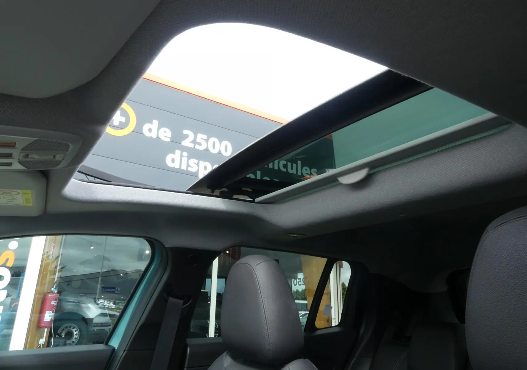 Vue intérieure du toit ouvrant électrique en verre du Jeep Avenger bleu métallisé 2024, avec sièges avant en cuir noir visibles.