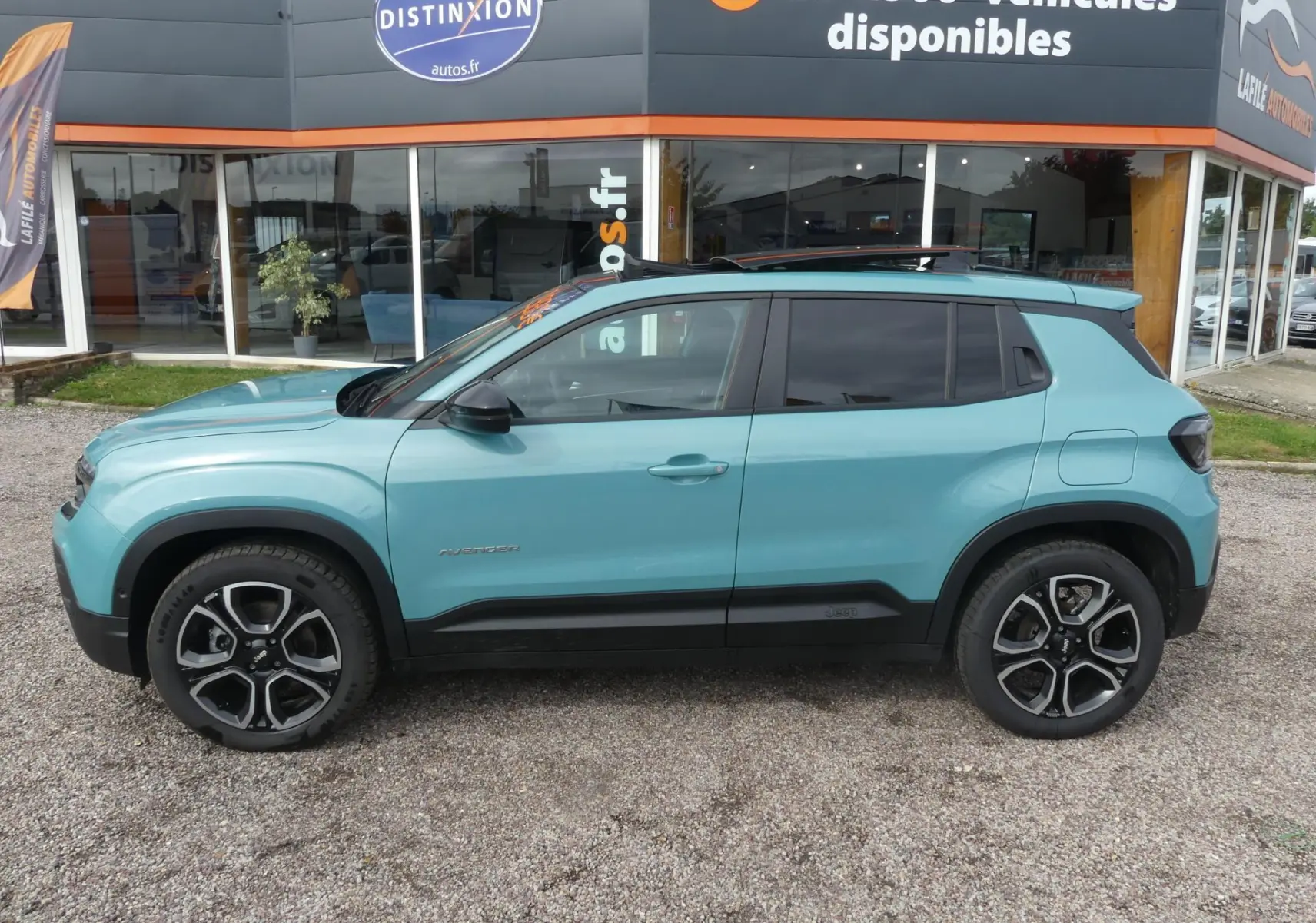Vue latérale gauche d'un Jeep Avenger 2024 bleu métallisé avec vitres surteintées et toit ouvrant en verre.