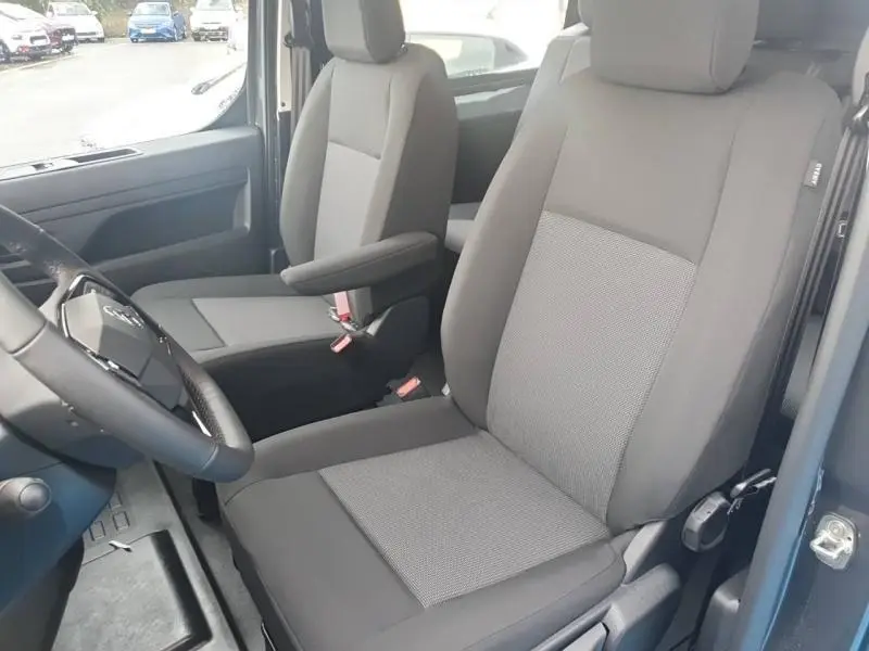 Vue intérieure côté conducteur du Citroën Jumpy 2025, sièges tissu bi-ton noir et gris avec accoudoir.