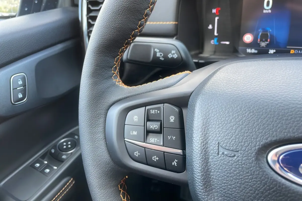 Gros plan sur le volant cuir noir avec surpiqûres orange du Ford Ranger Wildtrak 2025, boutons multifonctions visibles.