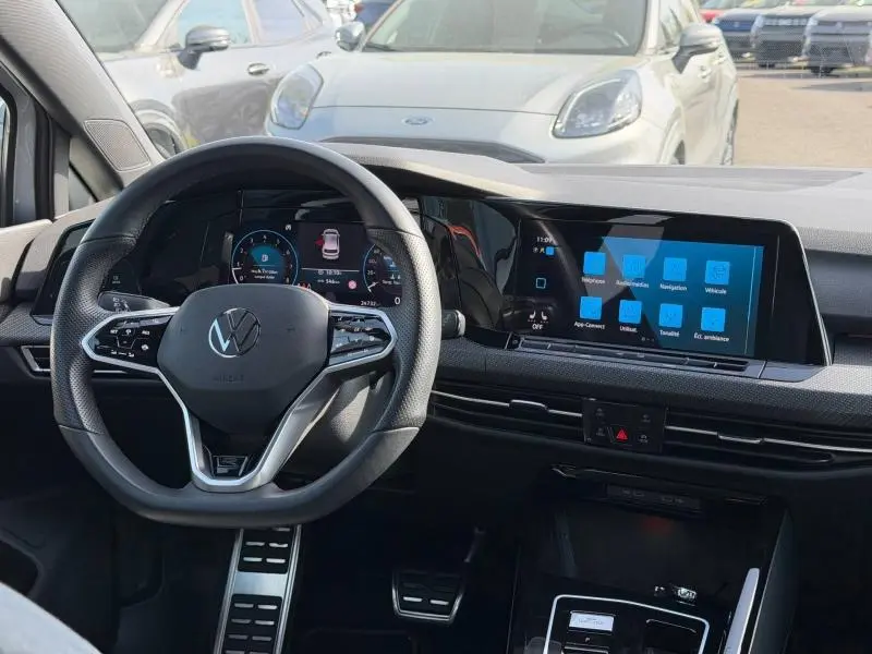 Vue intérieure centrée sur le volant multifonctions et l'écran tactile du tableau de bord d'une Volkswagen Golf 2024.