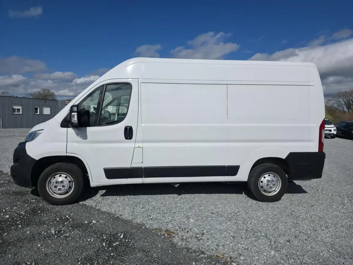Vue latérale droite d’un fourgon Opel Movano blanc avec portes latérale coulissante et jantes tôles grises sur sol gravillonné.