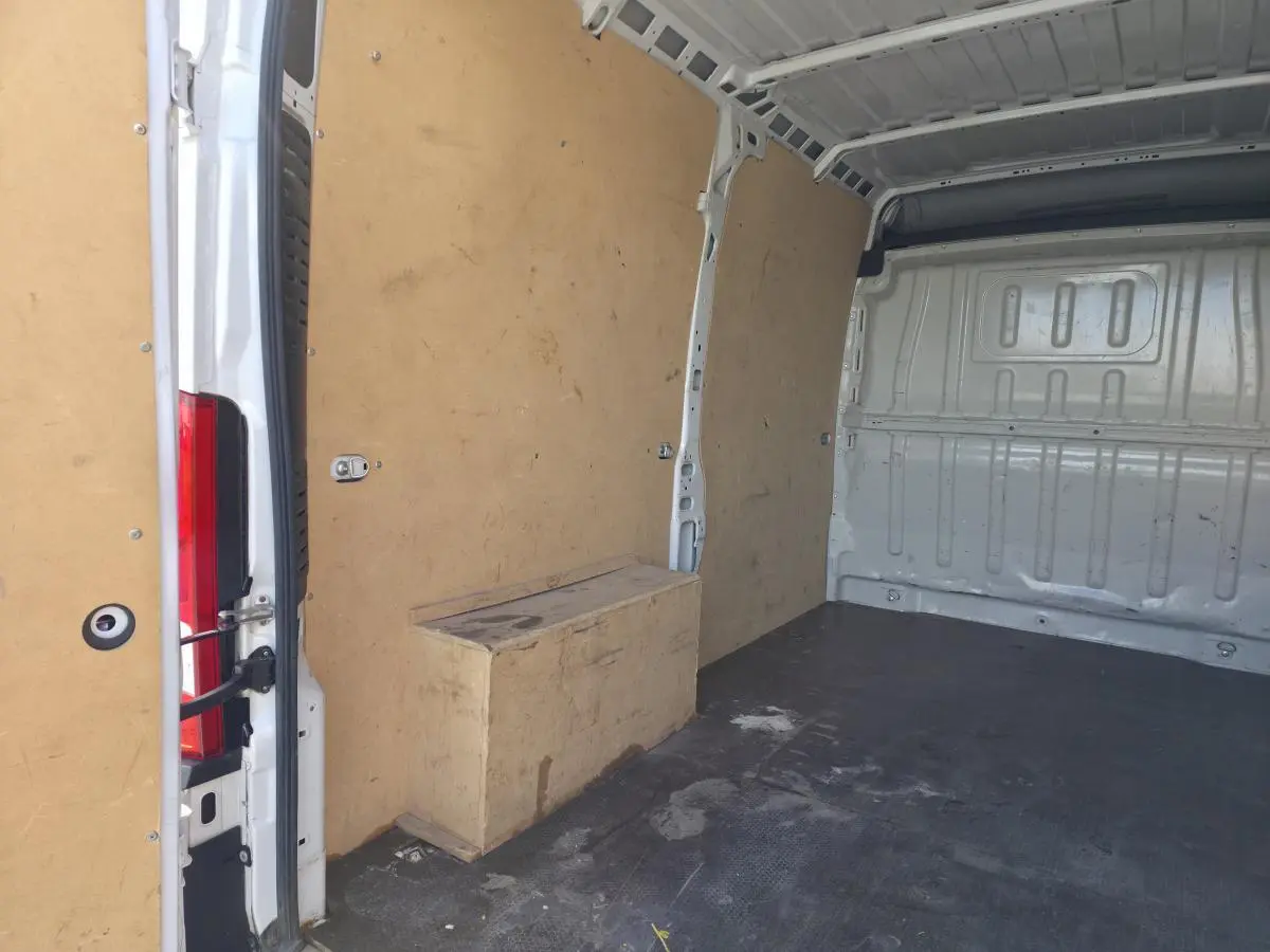 Vue intérieure arrière du fourgon Opel Movano blanc, montrant l'espace de chargement avec parois en bois et sol noir.