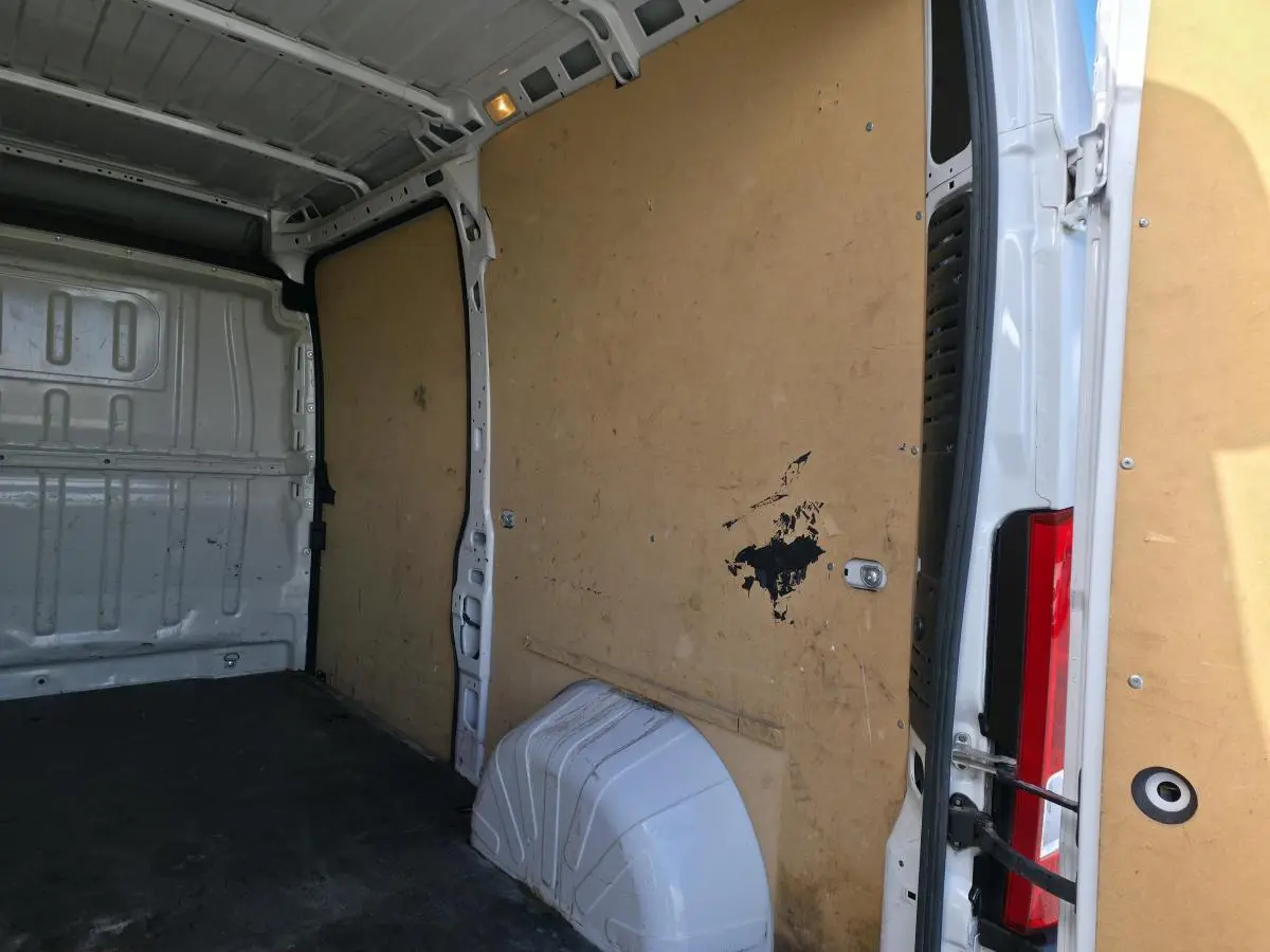 Intérieur du fourgon Opel Movano blanc, vue depuis l'arrière droit avec cloison en bois et plancher noir.