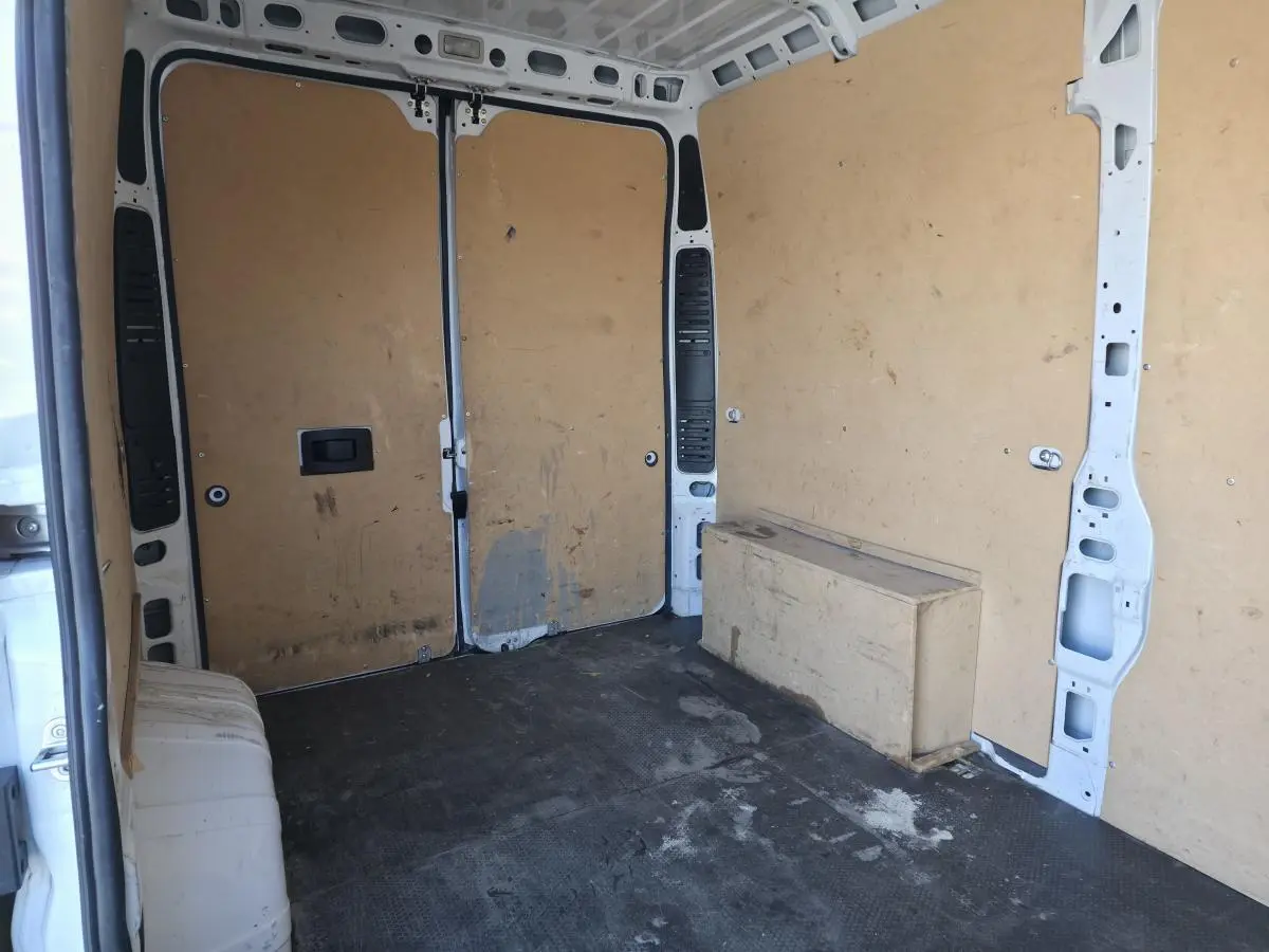 Vue intérieure arrière du fourgon Opel Movano blanc, montrant l'espace de chargement avec parois en bois et sol noir.