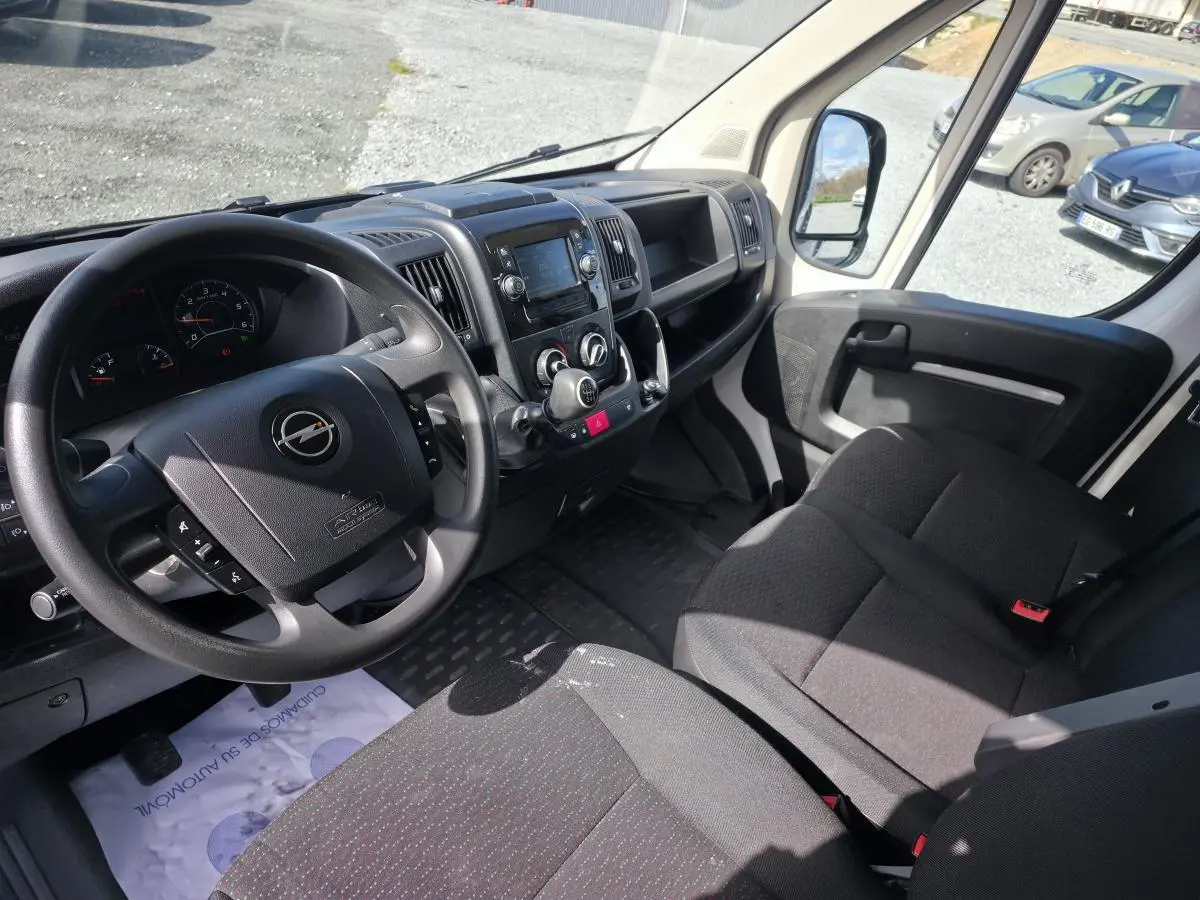 Vue intérieure côté conducteur de l’Opel Movano blanc, montrant le volant, tableau de bord et banquette passagers noire.