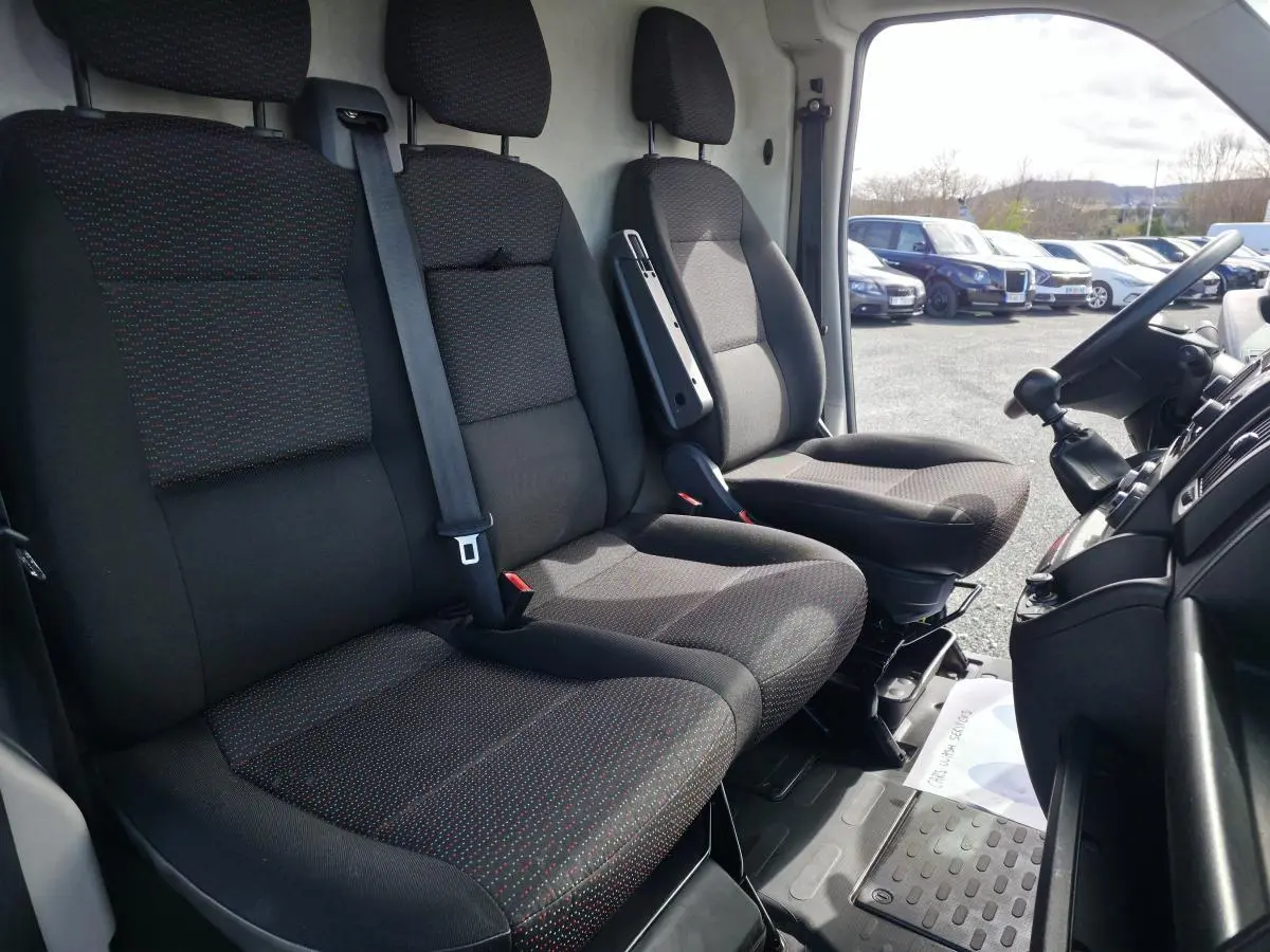 Vue intérieure côté conducteur de l’Opel Movano Fourgon 2022, sièges tissu noir avec motifs rouges et tableau de bord visible.
