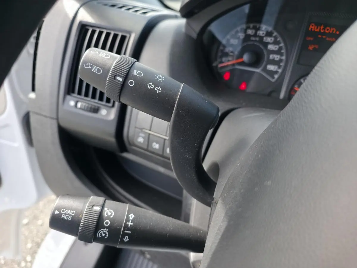 Gros plan sur les commandes au volant du côté gauche de l’Opel Movano Fourgon blanc, tableau de bord partiellement visible.
