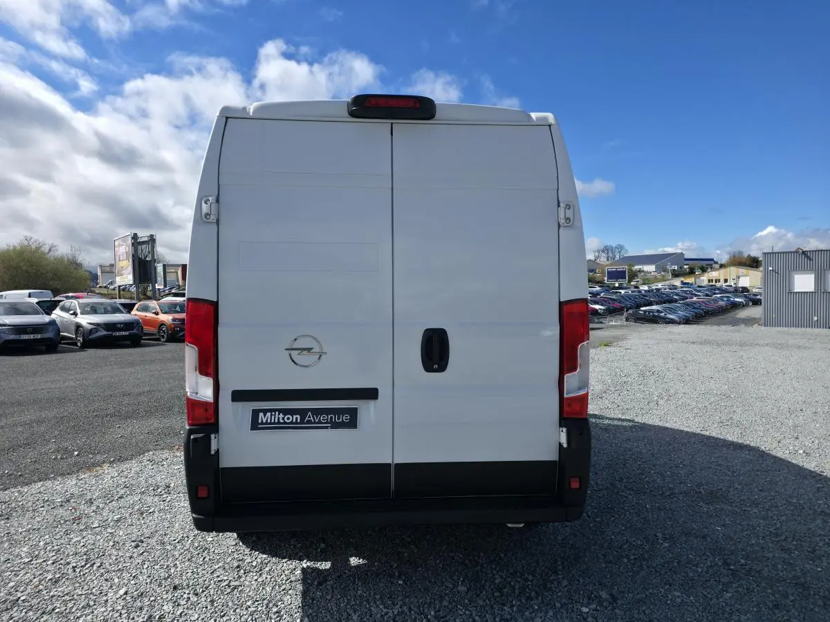 Vue arrière d’un utilitaire Opel Movano blanc avec portes battantes et feux rouges verticaux sur un parking.