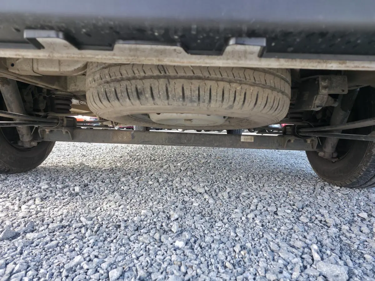 Vue en contre-plongée sous un Opel Movano Fourgon blanc, montrant la roue de secours et le châssis arrière sur sol gravillonné.