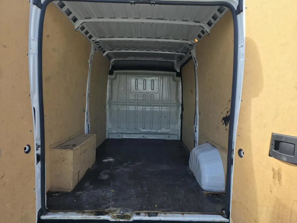 Vue intérieure arrière du fourgon blanc Opel Movano avec parois en bois et sol noir usé.