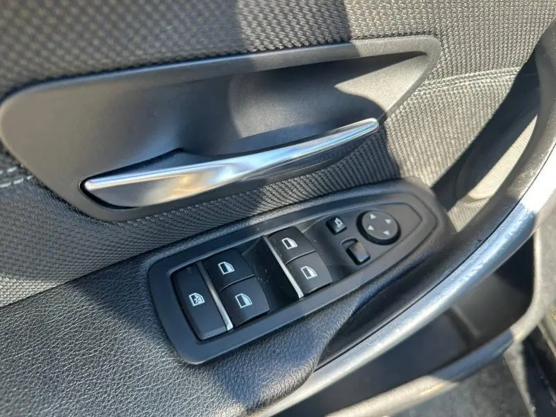 Gros plan sur la commande des vitres et la poignée intérieure côté conducteur de la BMW Série 4 Gran Coupe noire.