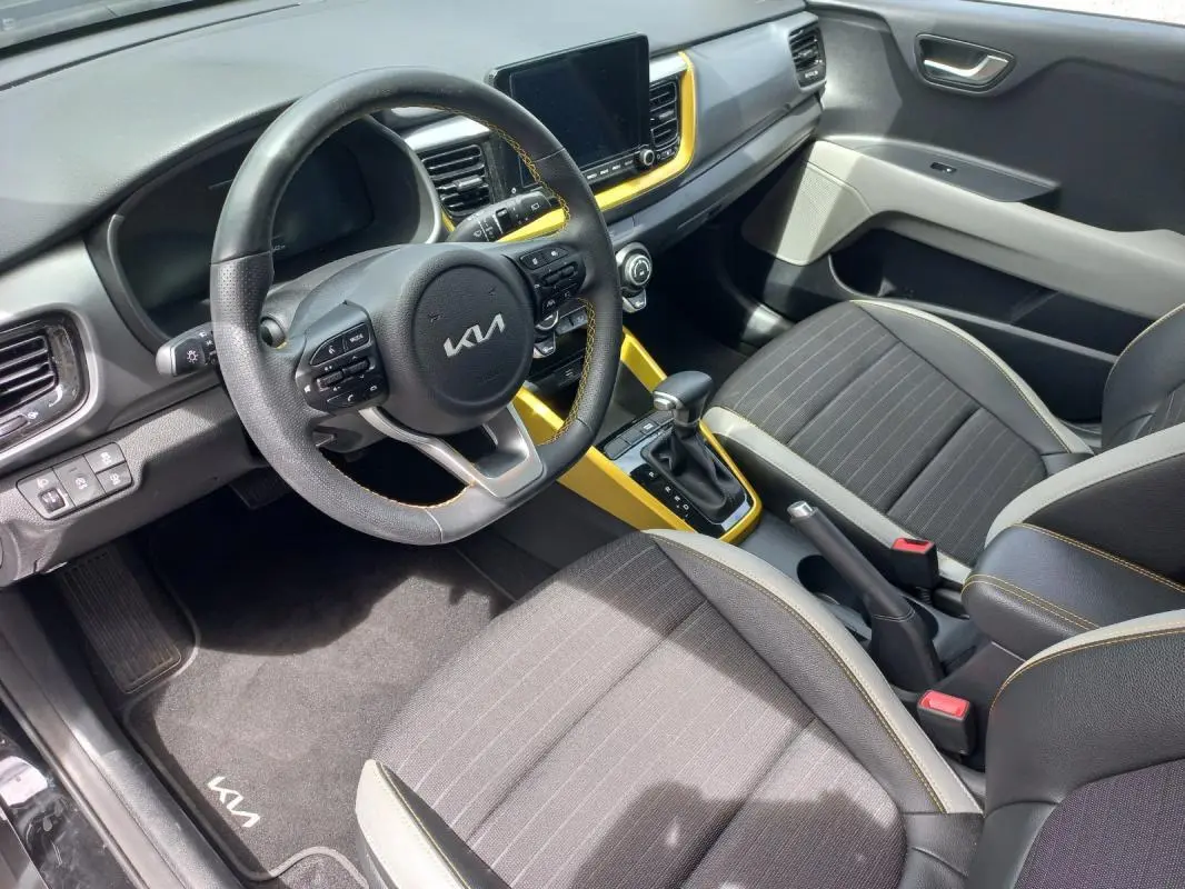Vue intérieure côté conducteur du Kia Stonic 2025 avec sellerie noire, volant multifonction et inserts jaunes autour de la console centrale.