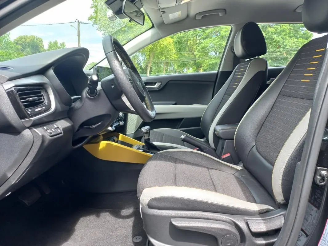 Vue intérieure côté conducteur du Kia Stonic noir 2025, avec sièges tissu noir et surpiqûres jaunes, console centrale jaune vif.