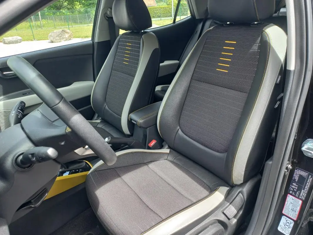Vue intérieure côté conducteur du Kia Stonic noir 2025, sièges tissu avec surpiqûres jaunes et détails gris.
