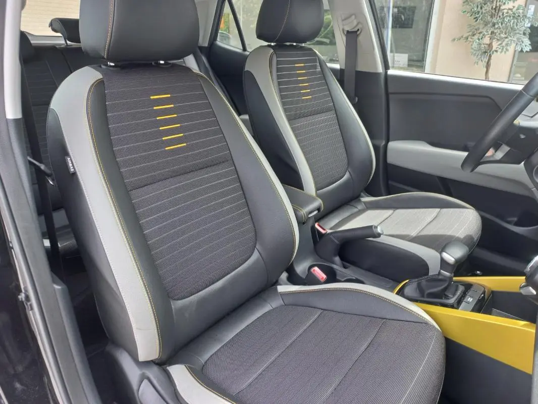 Vue intérieure des sièges avant du KIA Stonic 2025 noir, avec surpiqûres jaunes et console centrale jaune visible.