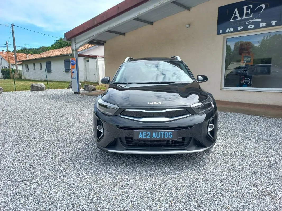 Vue de face d'un KIA STONIC noir 2025, avec calandre moderne et phares LED, stationné devant un bâtiment AE2 Autos.