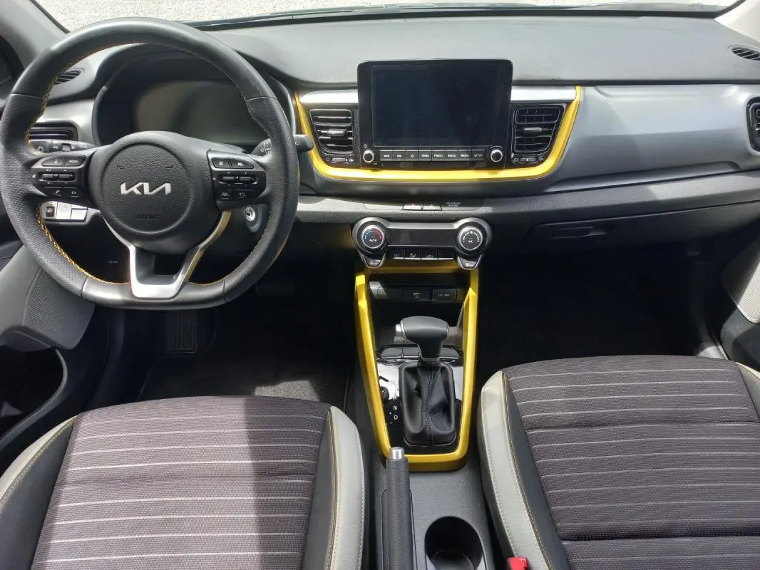 Vue intérieure avant du Kia Stonic 2025 noir, avec volant multifonction, écran central et contours jaunes autour de la console.