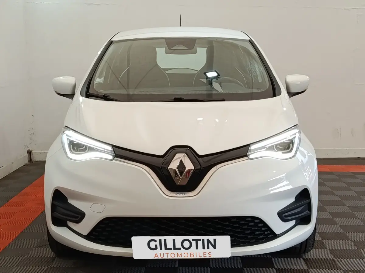 Vue de face de la Renault ZOE Business blanche 2021 avec phares LED allumés et calandre noire distinctive.